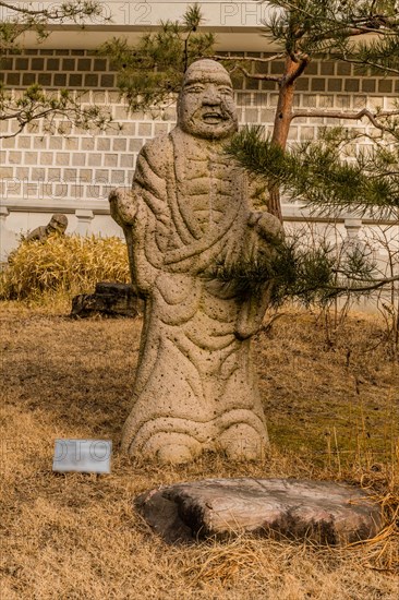 Stone carved statue of Buddhist deity kanakavatsa in front of white wall in garden in South Korea