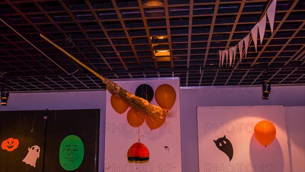 Wooden wicker broom hanging from ceiling with orange balloons and hand made Halloween decorations hanging on the wall in South Korea