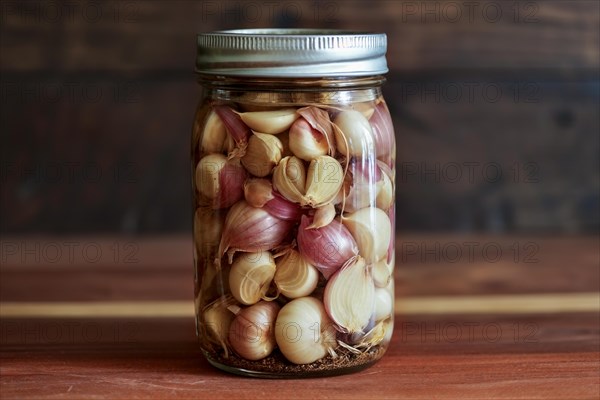 A glass jar filled with pickled garlic cloves and shallots on a rustic wooden background, KI generated, AI generated