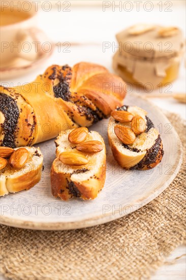 Homemade sweet bun with honey almonds and cup of green tea on a white wooden background and linen textile. side view, close up, selective focus