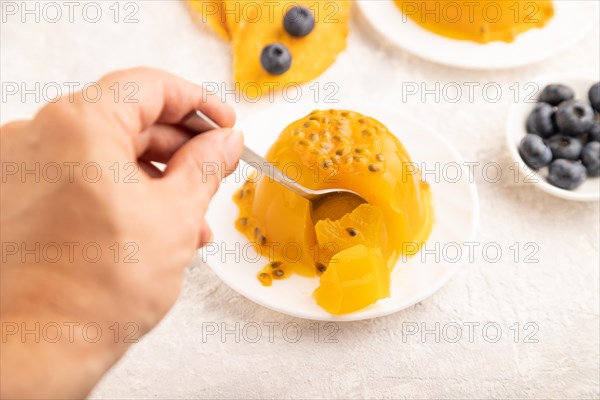 Mango and passion fruit jelly with blueberry on gray concrete background with hand. side view, close up, selective focus