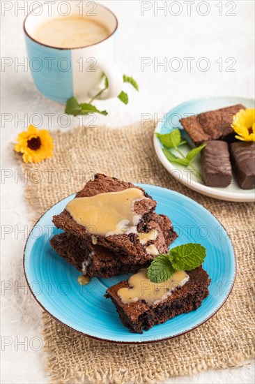 Chocolate brownie with caramel sauce with a cup of coffee on gray concrete background and linen textile. side view, close up
