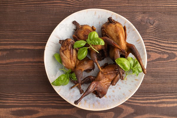Smoked quails with herbs and spices on a ceramic plate on a brown wooden background. Top view, flat lay