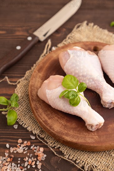 Raw chicken legs with herbs and spices on a wooden cutting board on a brown wooden background and linen textile. Side view, close up, selective focus