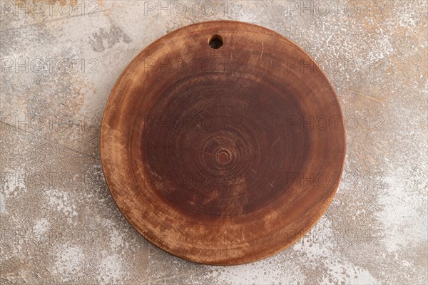 Empty round wooden cutting board on brown concrete background. Top view, close up, flat lay