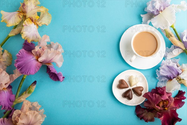 Cup of cioffee with chocolate candies, lilac and purple iris flowers on blue pastel background. top view, flat lay, copy space, still life. Breakfast, morning, spring concept