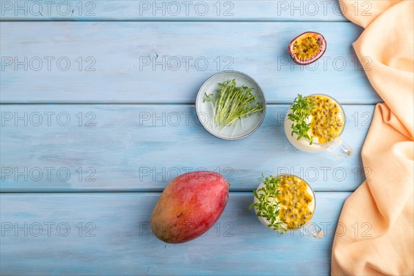Mango yogurt with passionfruit and cilantro microgreen in glass on blue wooden background with orange linen textile. Top view, flat lay, copy space