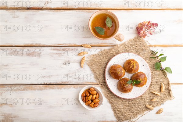 Homemade traditional turkish dessert sekerpare with almonds and honey, cup of green tea on white wooden background and linen textile. top view, flat lay, copy space