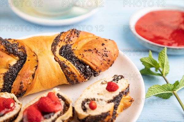 Homemade sweet bun with strawberry jam and cup of green tea on a blue wooden background. side view, close up, selective focus