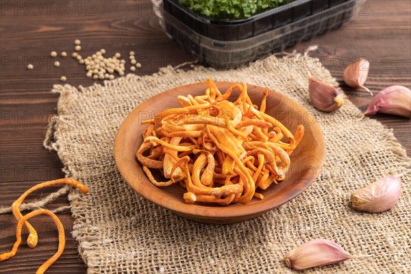 Fresh Cordyceps militaris mushrooms on brown wooden background with microgreen, herbs and spices. Side view, close up