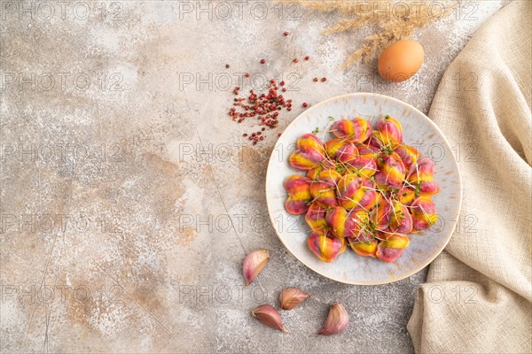 Rainbow colored dumplings with pepper, herbs, microgreen on brown concrete background and linen textile. Top view, flat lay, copy space