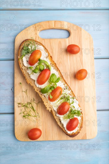 Long white bread sandwich with cream cheese, tomatoes and microgreen on blue wooden background. top view, flat lay, close up