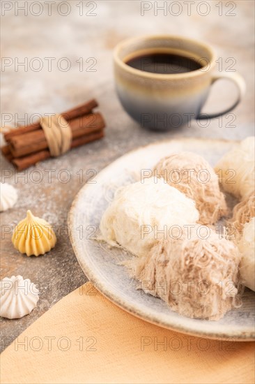 Traditional arabic sweets pishmanie and a cup of coffee on brown concrete background and orange linen textile. side view, close up, selective focus