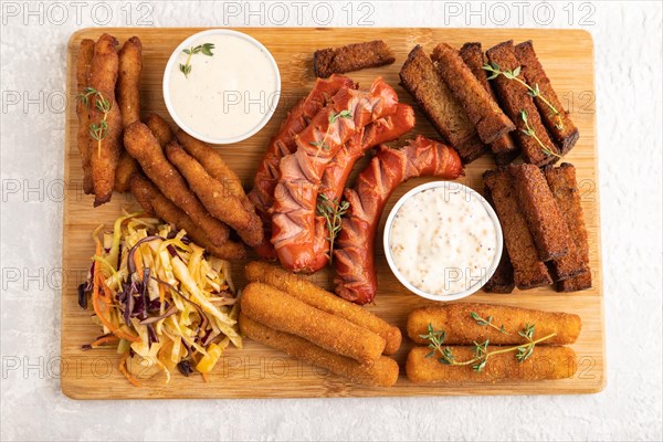 Set of snacks: sausages, nuggets, cheese sticks, toast, cabbage salad on a cutting board on a gray concrete background. Top view, flat lay, close up