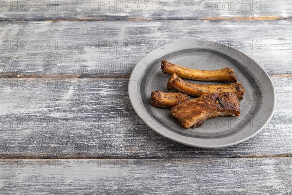 Pork ribs on a wooden plate on a gray wooden background. Side view, close up, copy space