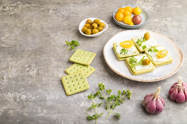 Green cracker sandwiches with cream cheese and cherry tomatoes on gray concrete background. side view, copy space