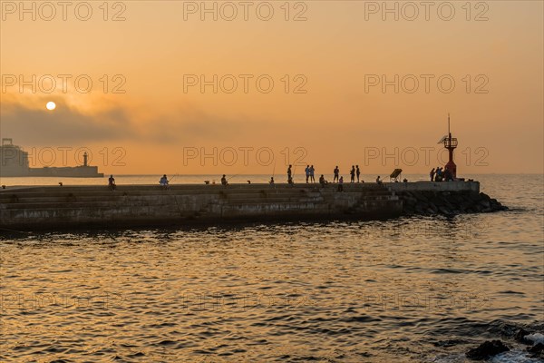 Unidentified people fishing of concrete pier at sunset in Jeju, South Korea, Asia