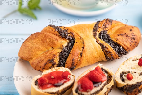 Homemade sweet bun with strawberry jam and cup of green tea on a blue wooden background. side view, close up, selective focus