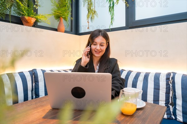 Casual young businesswoman talking to the mobile while using laptop in a cafeteria