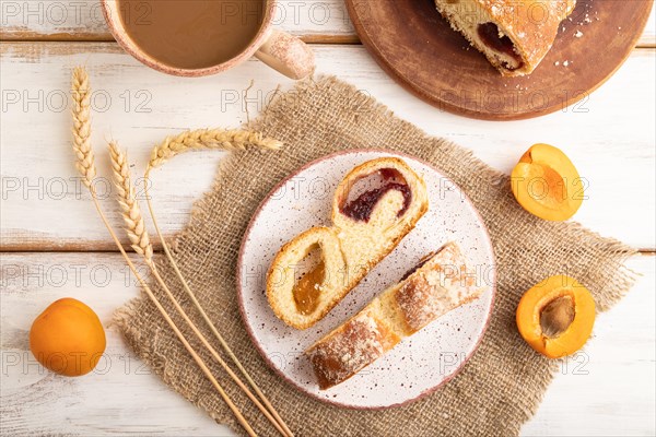 Homemade sweet bun with apricot jam and cup of coffee on white wooden background and linen textile. top view, flat lay, close up