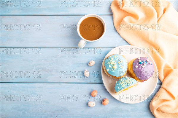Purple and blue glazed donut and cup of coffee on blue wooden background and orange linen textile. top view, flat lay, copy space. Breakfast, morning, concept