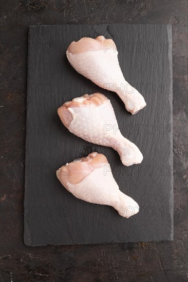 Raw chicken legs on a black slate cutting board on a black concrete background. Top view, flat lay, close up