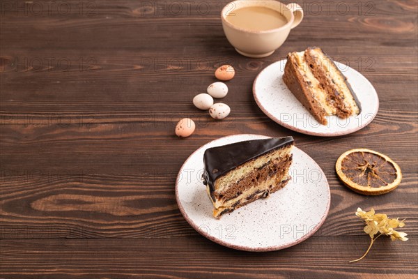 Chocolate biscuit cake with caramel cream, cup of coffee on brown wooden background. side view, copy space