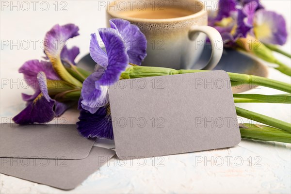 Gray business card with cup of cioffee and iris flowers on white concrete background. side view, copy space, still life. Breakfast, morning, spring concept