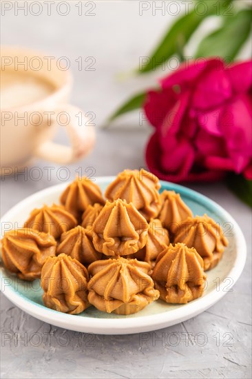 Homemade soft caramel fudge candies on blue plate and cup of coffee on gray concrete background, peony flower decoration. side view, close up, selective focus