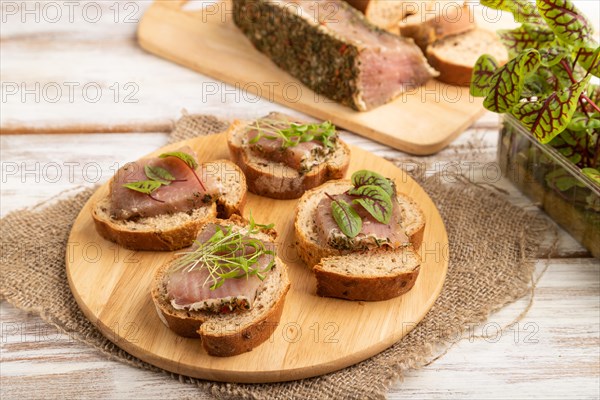 Bread sandwiches with jerky salted meat, sorrel and cilantro microgreen on white wooden background and linen textile. side view, close up