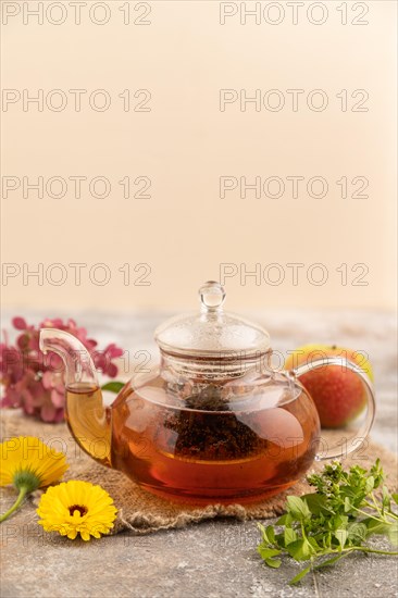 Red tea with herbs in glass teapot on brown concrete background and linen textile. Healthy drink concept. Side view, close up, selective focus
