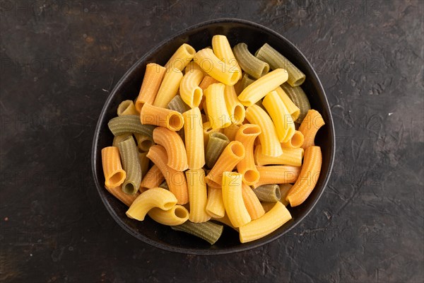 Rigatoni colored raw pasta with tomato, eggs, spices, herbs on black concrete background. Top view, flat lay