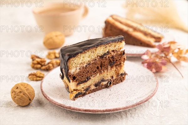 Chocolate biscuit cake with caramel cream and walnuts, cup of coffee on gray concrete background. side view, close up, selective focus