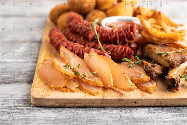 Set of snacks: sausages, fried potatoes, meat balls, dumplings, basturma on a cutting board on a gray wooden background. Side view, close up, selective focus
