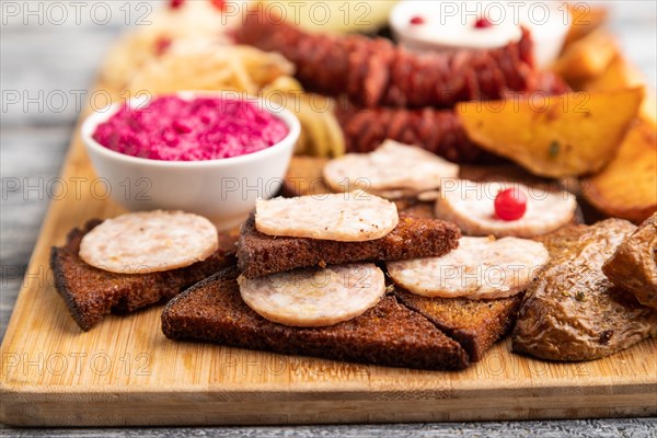 Set of snacks: sausages, toast, sauerkraut, marinated onion and cucumber, baked potato on a cutting board on a gray wooden background. Side view, close up, selective focus
