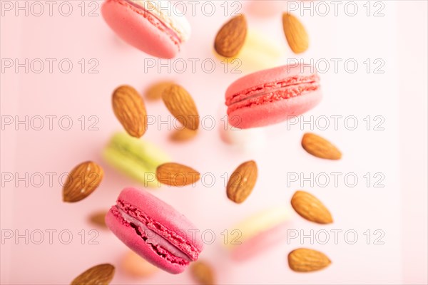 Multicolored flying macaroons and almonds frozen in the air on blurred pink background. top view, flat lay, close up. Breakfast, morning, concept