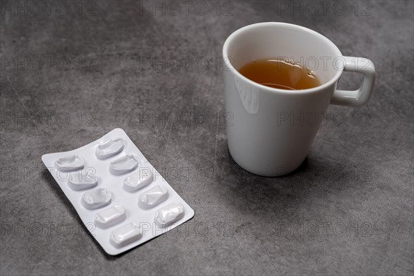 A blister pack with pills next to a cup of tea on a grey background, top view, studio shot, Germany, Europe