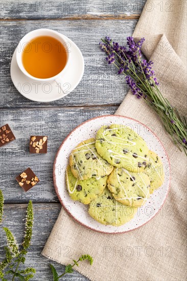 Green cookies with chocolate and mint on ceramic plate with cup of green tea and linen textile on gray wooden background. top view, flat lay, close up