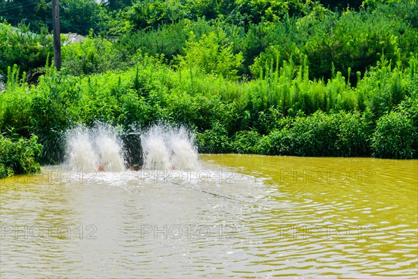 Paddle-wheels being used to aerate rural pond with green foliage on shoreline