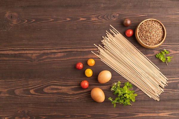 Japanese buckwheat soba noodles with tomato, eggs, spices, herbs on brown wooden background. Top view, flat lay, copy space