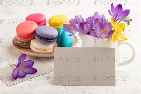 Gray paper business card mockup with spring snowdrop crocus flowers and multicolored macaroons on gray concrete background. Blank, business card, side view, copy space, still life. spring concept