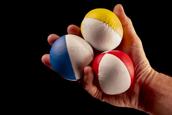 Male hand holding 3 colourful juggling balls, black background, studio shot, Germany, Europe