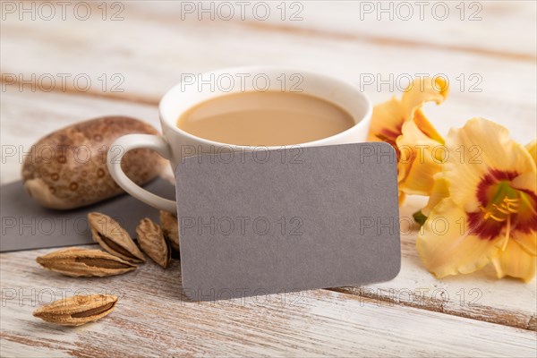 Gray paper business card mockup with orange day-lily flower and cup of coffee on white wooden background. Blank, side view, copy space, still life. spring concept