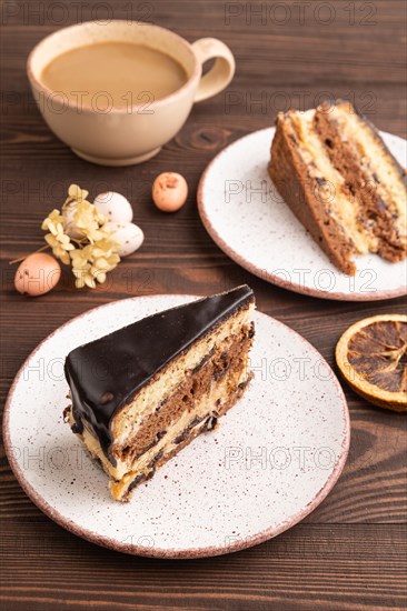 Chocolate biscuit cake with caramel cream, cup of coffee on brown wooden background. side view, close up