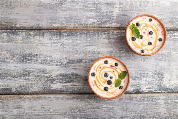 Yoghurt with bilberry and caramel in clay bowl on gray wooden background. top view, flat lay, copy space