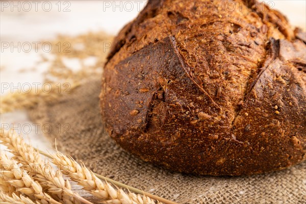 Fresh homemade golden grain bread with ears of wheat and rye on white wooden background and linen textile. side view, close up, selective focus