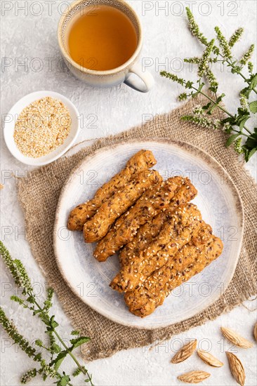 Crumble cookies with seasme and almonds on ceramic plate with cup of green tea and linen textile on gray concrete background. top view, flat lay, close up