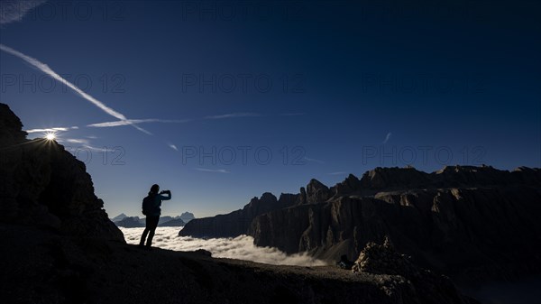 Mobile phone photographer on ridge with Dolomites mountains in the background, Corvara, Dolomites, Italy, Europe