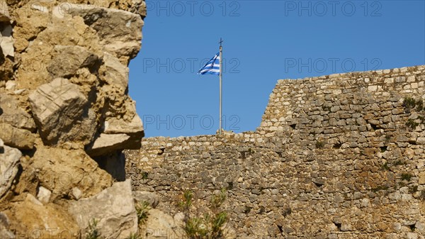Part of an old fortress wall with a waving Greek flag and blue sky, Chlemoutsi, High Medieval Crusader Castle, Kyllini Peninsula, Peloponnese, Greece, Europe