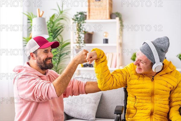 Disabled man and friend feeling happy and giving each other a fist bump while listening to music at home
